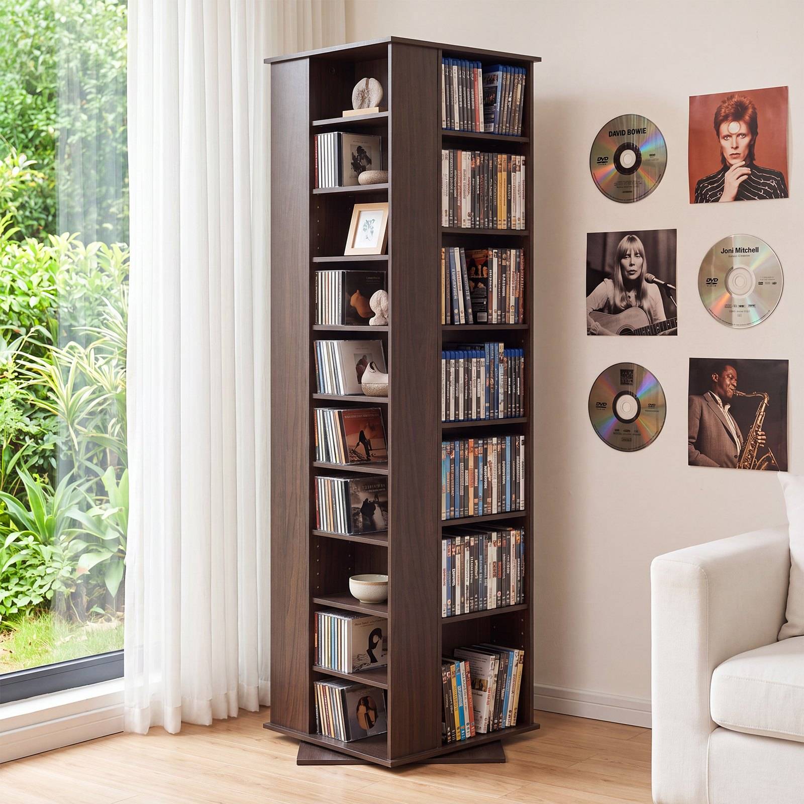 Ein hoher dunkler Holzregal mit rotierender Funktion, gefüllt mit DVDs und Büchern neben einem Fenster in einem hellen Wohnzimmer, mit Musikalbum-Kunstwerken an der Wand.