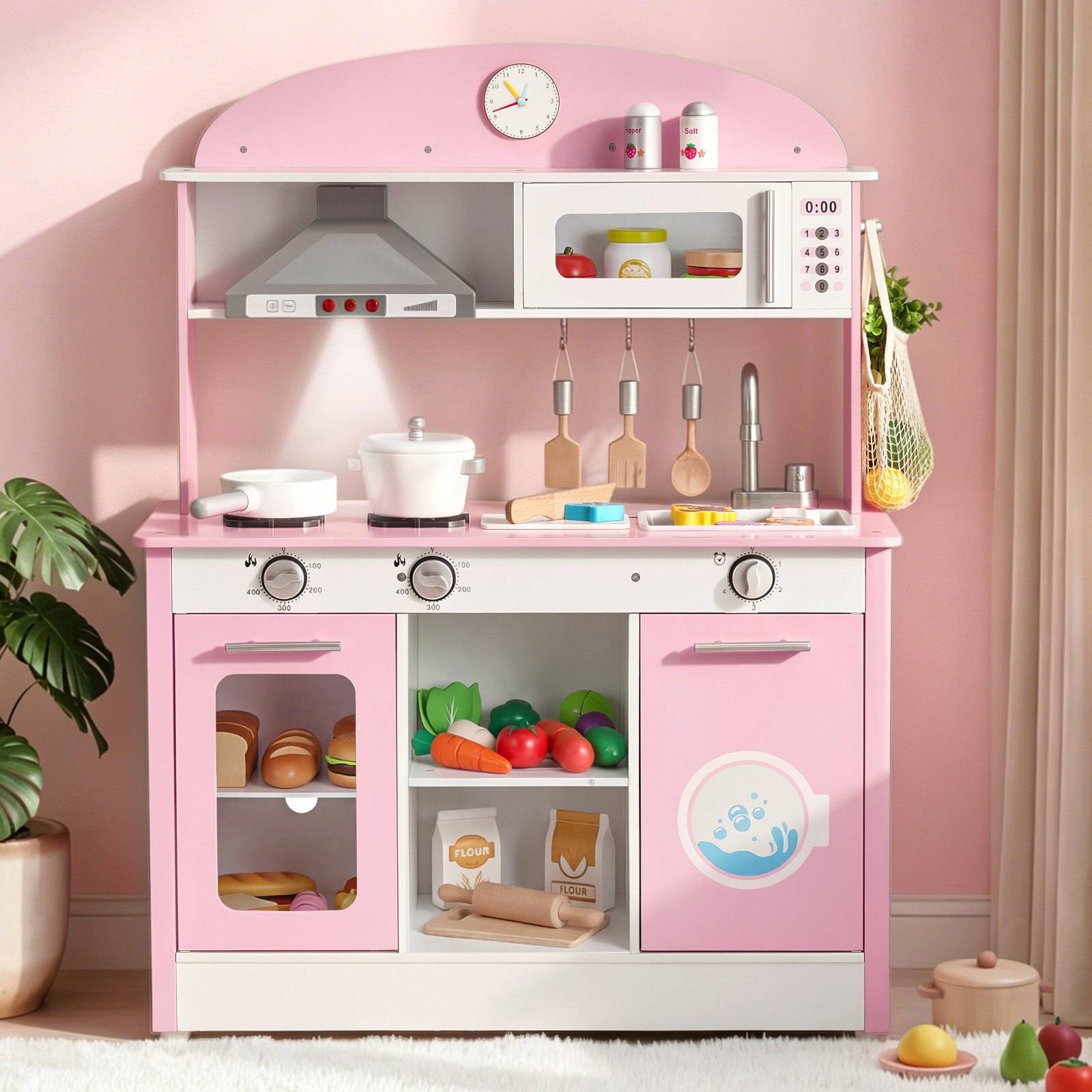 Rosa Spielzeugküche mit Herd, Ofen, Mikrowelle, Küchengeräten und Spielzeugessen, gestaltet als Kinderküche zum Rollenspiel vor einer rosa Wand.