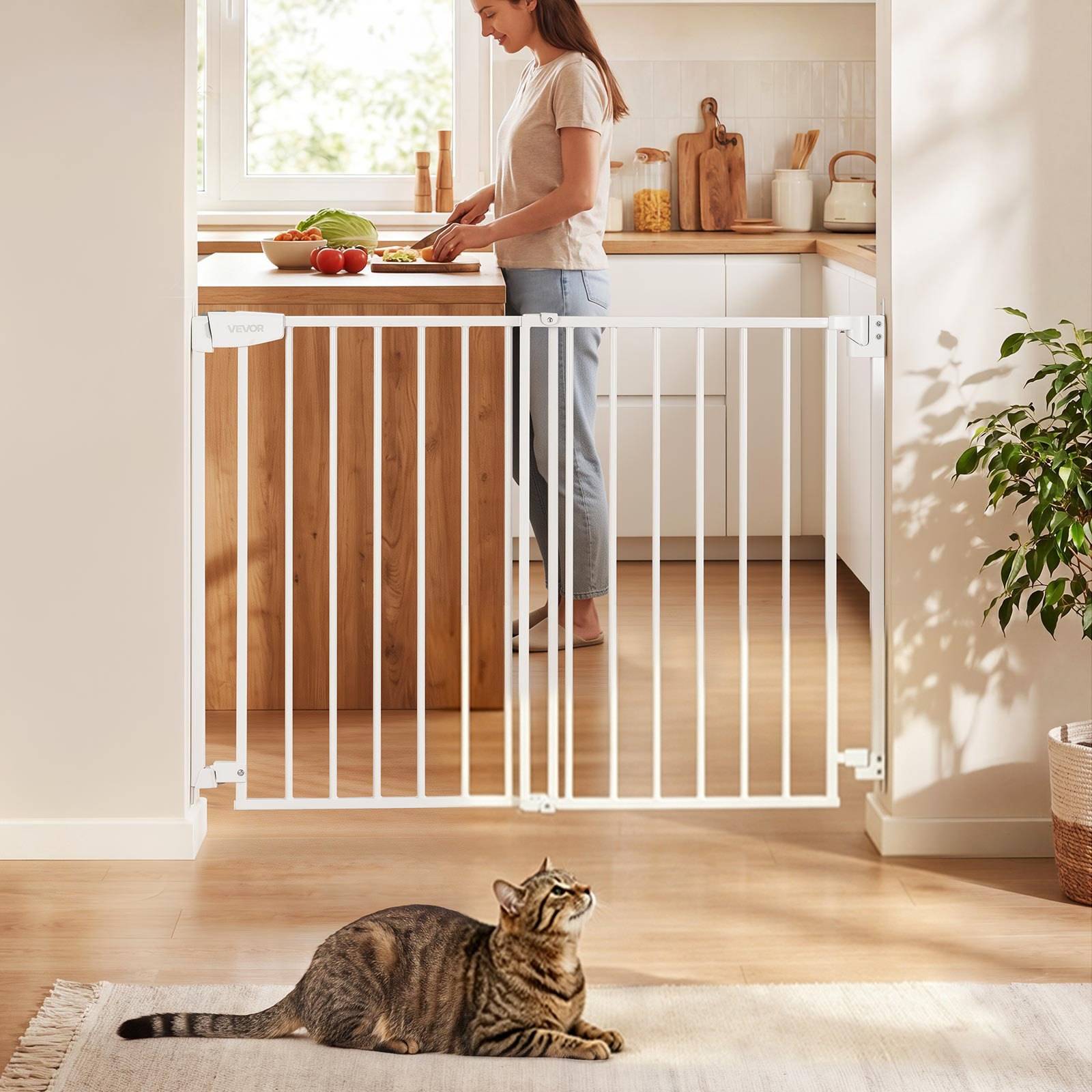 Frau, die Essen in einer Küche hinter einem weißen Sicherheitsgitter zubereitet, mit einer gestromten Katze, die auf dem Boden davor liegt.