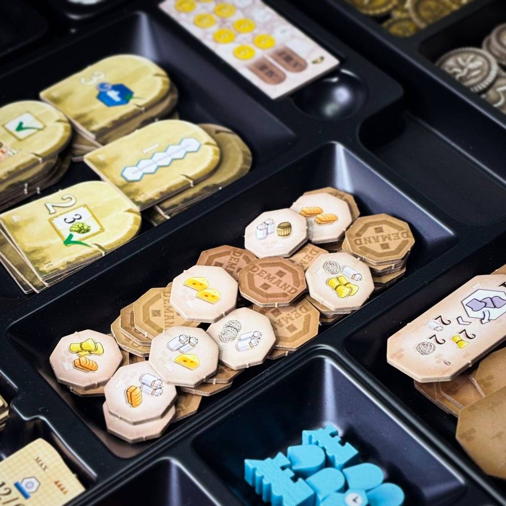 Ein Brettspiel-Organizer-Tablett mit Stapeln von sechseckigen hölzernen Ressourcentokens und Markern, einschließlich Symbolen für Nahrung, Werkzeuge, Stein und Weizen.