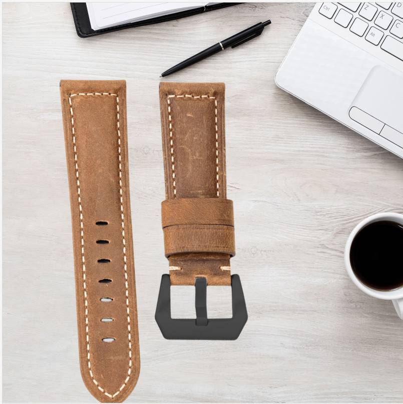 Braunes Lederuhrband mit schwarzer Schnalle, auf einem Schreibtisch neben einem Laptop, Stift, Tablet und einer Kaffeetasse abgebildet.