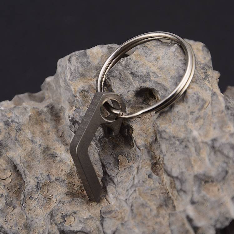 Silberner Schlüsselanhänger mit einem dunklem Metallanhänger mit eckigen Formen, der auf einem rauen grauen Stein vor dunklem Hintergrund ruht.