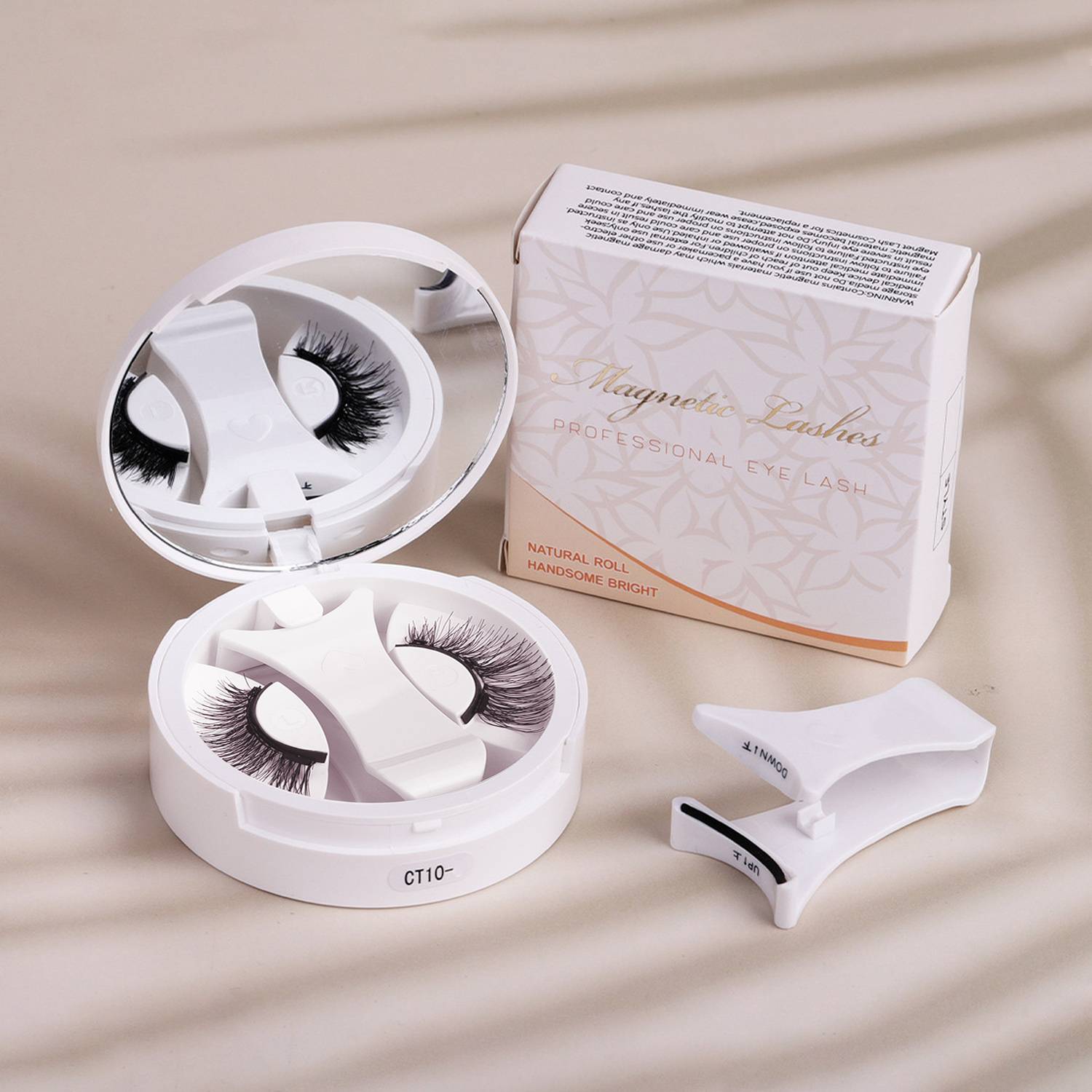 Magnetische künstliche Wimpern in einem runden Behälter mit Verpackungsbox und Applikator-Werkzeug auf einer beigen Oberfläche.