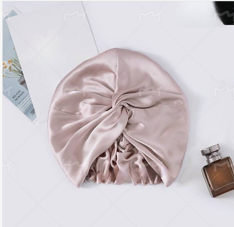 Hellrosa Satin-Turban-Mütze mit gesammeltem vorderen Knoten, gezeigt auf einer weißen Oberfläche mit einer Parfümflasche und einer Magazinseite in der Nähe.