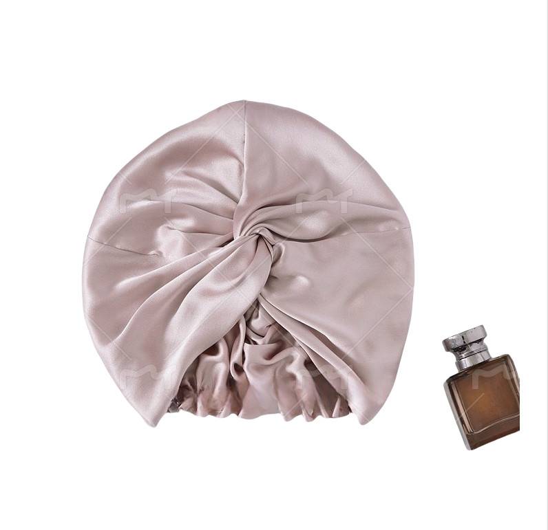 Beige Satin-Duschhaube mit geraffter Vorderbindung, gezeigt mit einer kleinen braunen Parfümflasche auf weißem Hintergrund.