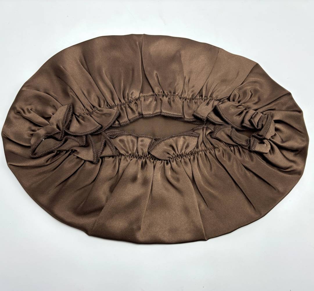 Braunes Satinovalem Haube mit elastischen gekräuselten Kanten, flach auf weißem Hintergrund ausgelegt.
