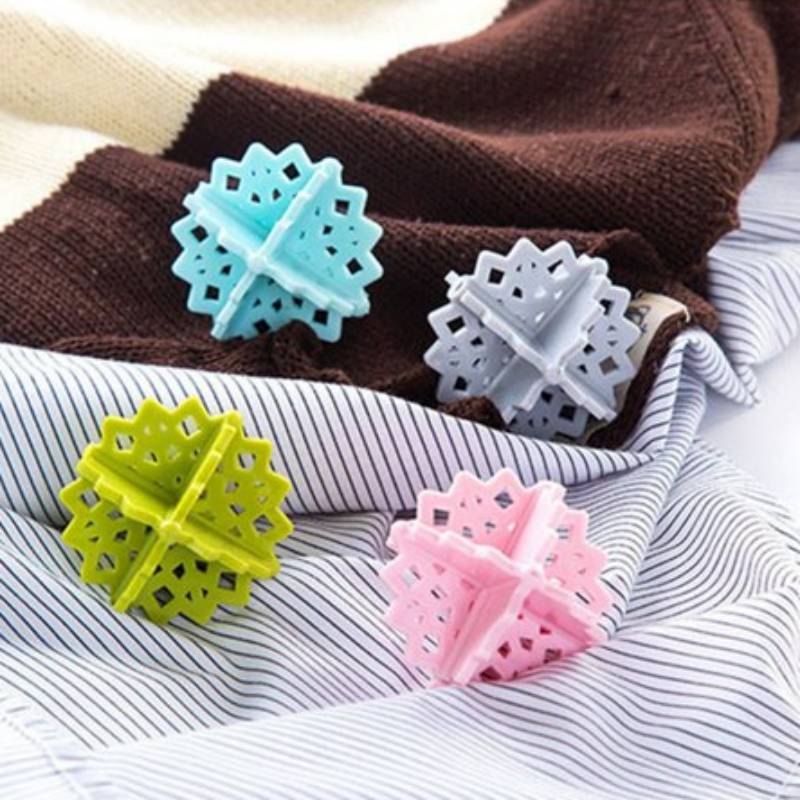 Vier bunte schneeflockenförmige Wäschebälle ruhen auf gefalteten Stoffen und werden wahrscheinlich verwendet, um Kleidung zu erweichen und statische Aufladung in der Wäsche zu reduzieren.