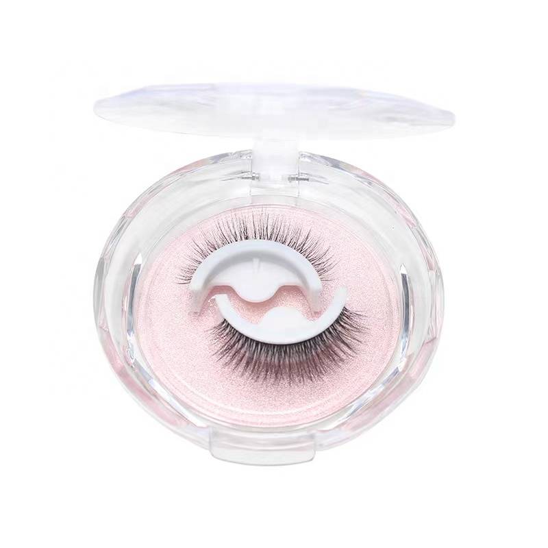 Transparente Kontaktlinsendose mit rosa Kontaktlinsen und einem Paar künstliche Wimpern darin, geschlossen gegen einen weißen Hintergrund dargestellt