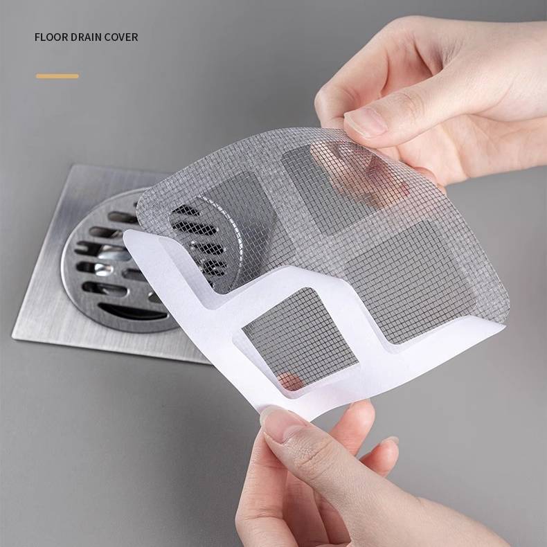 Hände halten einen Maschenrost-Ablaufdeckel über einem Metallablaufgitter, wobei ein abnehmbarer Filter zum Auffangen von Schmutz sichtbar ist.