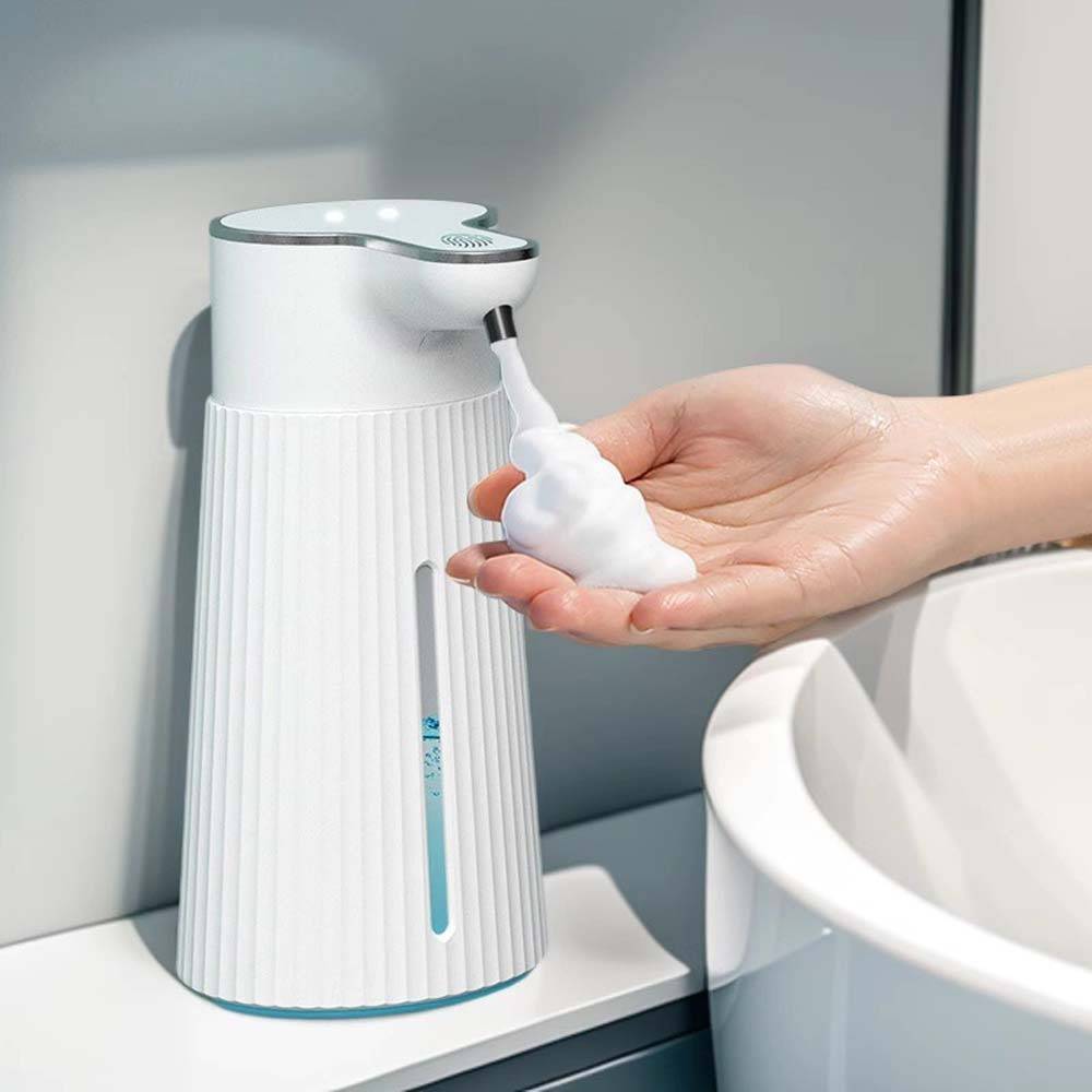 Hand wird aus einem weißen berührungslosen Seifenspender neben einem Waschbecken mit Schaumseife dispensiert.