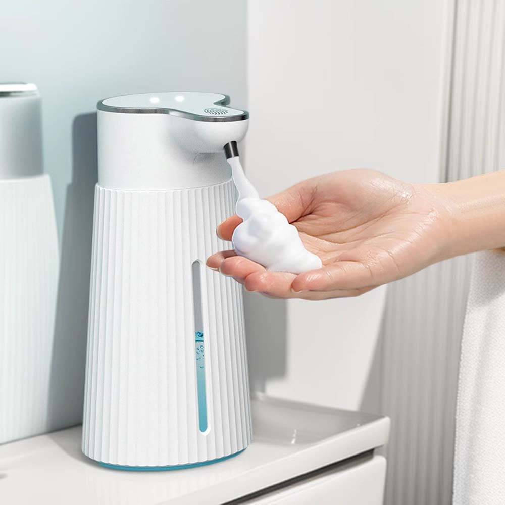 Eine Hand entnimmt Schaum-Seife aus einem weißen automatischen Seifenspender auf einer Badezimmerablage.