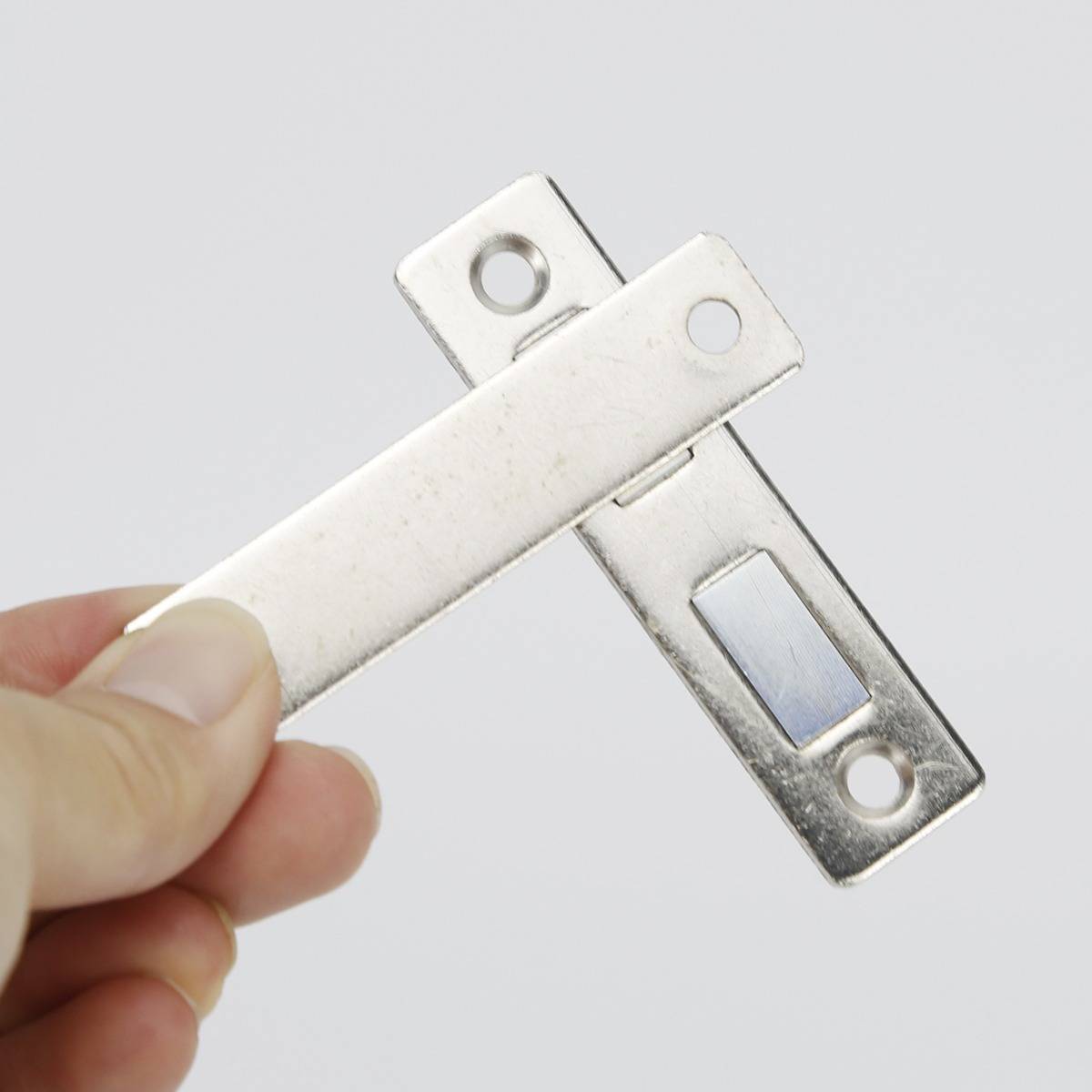 Hand, die eine weiße und silberne Metallklinke oder ein Halter mit zwei Schraubenlöchern gegen einen schlichten hellgrauen Hintergrund hält.