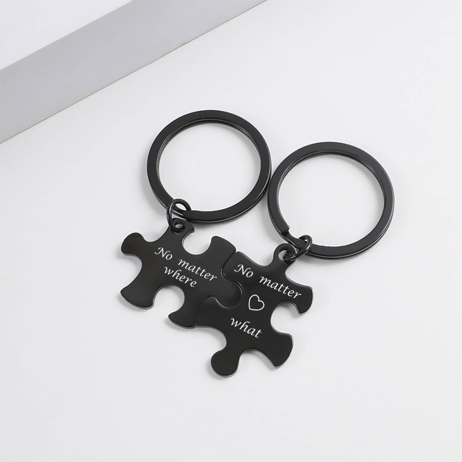 Zwei schwarze Puzzle-Anhänger an Metallringen mit den Gravuren „Egal wo" und „Egal was"" auf weißem Hintergrund.