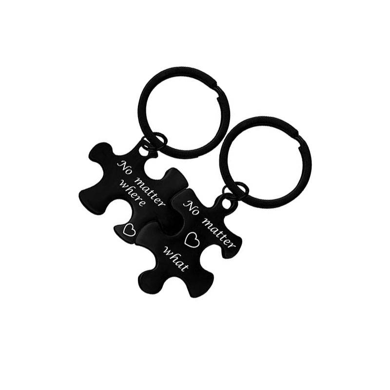 Zwei schwarze Puzzle-Anhänger mit Ringen, jeweils graviert mit „Egal wo" und „Egal was"" plus einem Herzsymbol.