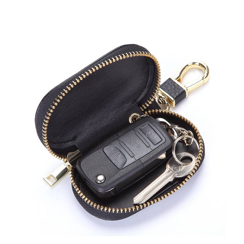 Offene schwarze Reißverschluss-Schlüsseltasche mit goldenem Beschlag, enthält eine Autoschlüsselanhänger und metallischen Schlüssel, gezeigt auf weißem Hintergrund.