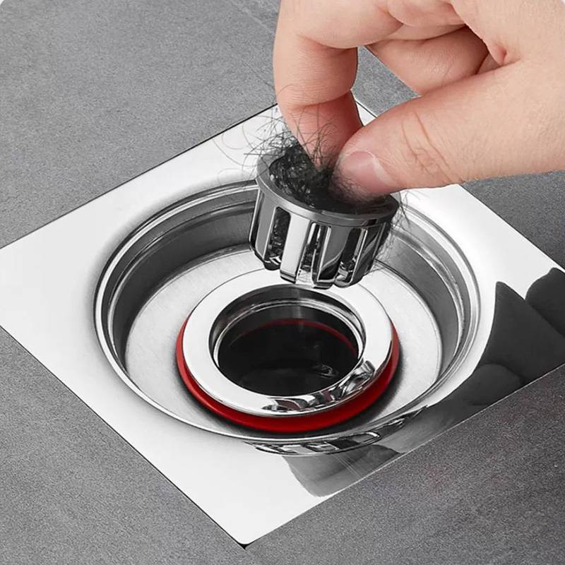 Hand entfernt Haare aus einem Metallsiebeinsatz in einem Waschbecken und zeigt, wie ein verstopfter Dusch- oder Waschbeckenablauf gereinigt wird.