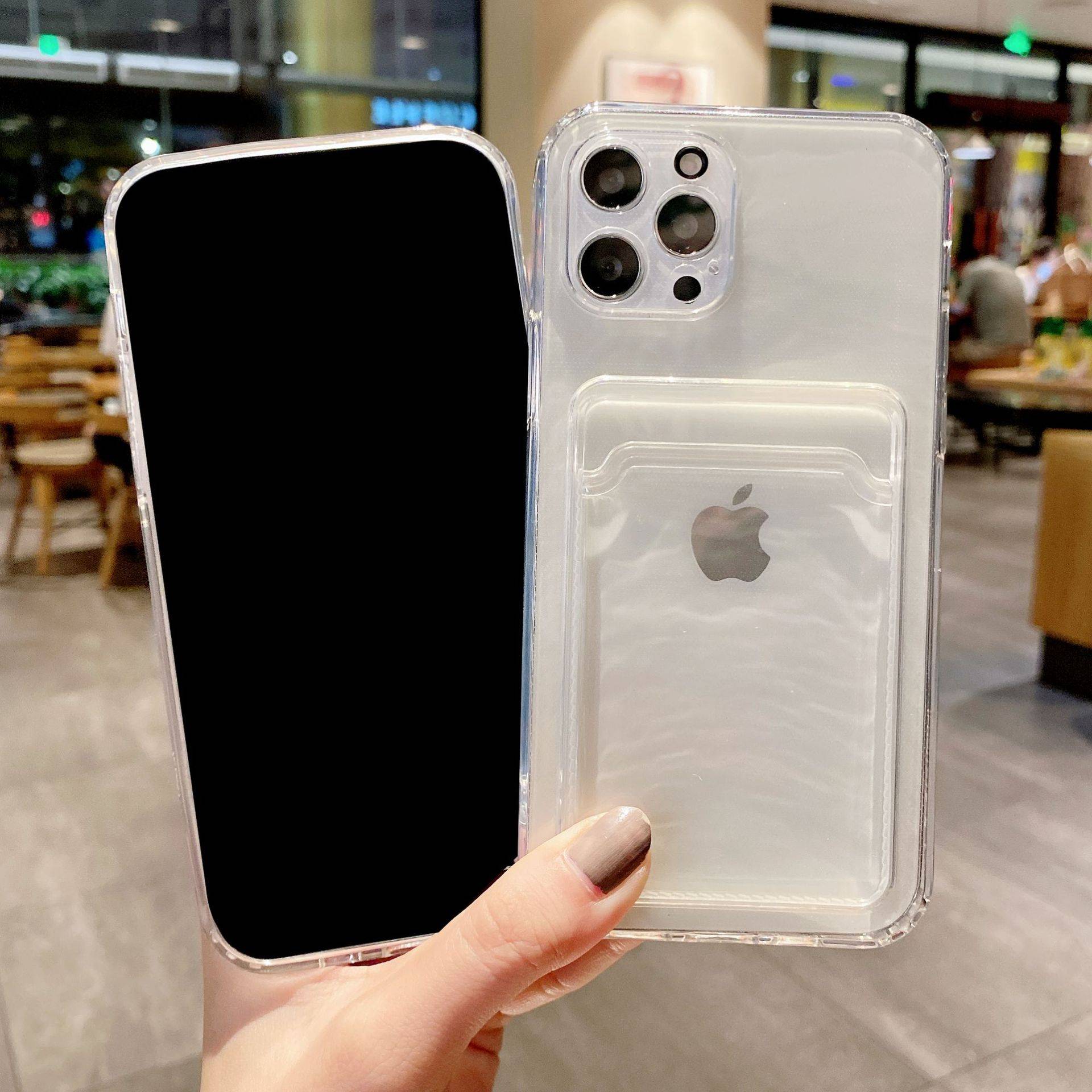 Eine Hand hält zwei transparente iPhone-Hüllen in einem Geschäft: eine Vorderseite-Schutzhülle mit schwarzem Bildschirmeinsatz und eine, die die Rückseite mit Apple-Logo und dreifachem Kamera-Ausschnitt zeigt.