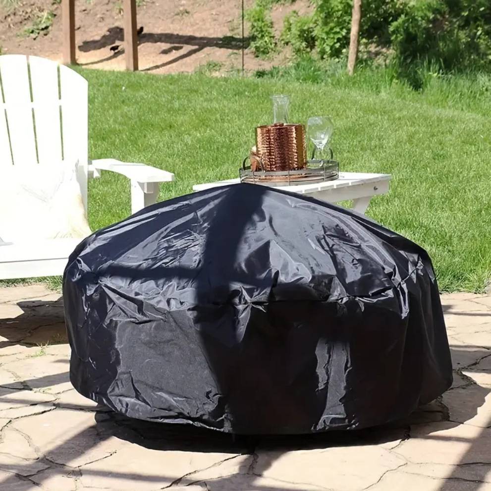 Schwarze abgedeckte Feuerstelle oder Grill im Freien auf einer Steinterrasse neben einem weißen Stuhl und einem kleinen Beistelltisch in einem sonnigen Hinterhof