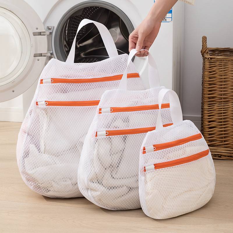 Drei Mesh-Wäschesäcke mit orangefarbenen Reißverschlüssen werden aus einer Frontlader-Waschmaschine in einer Waschküche entnommen.