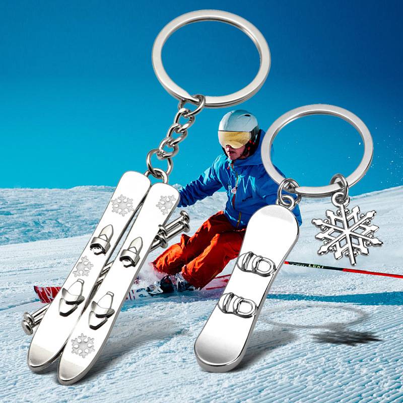 Skifahrer auf verschneiter Piste mit drei silbernen Schlüsselanhängern in Form von Skiern und einer Schneeflocke im Vordergrund.