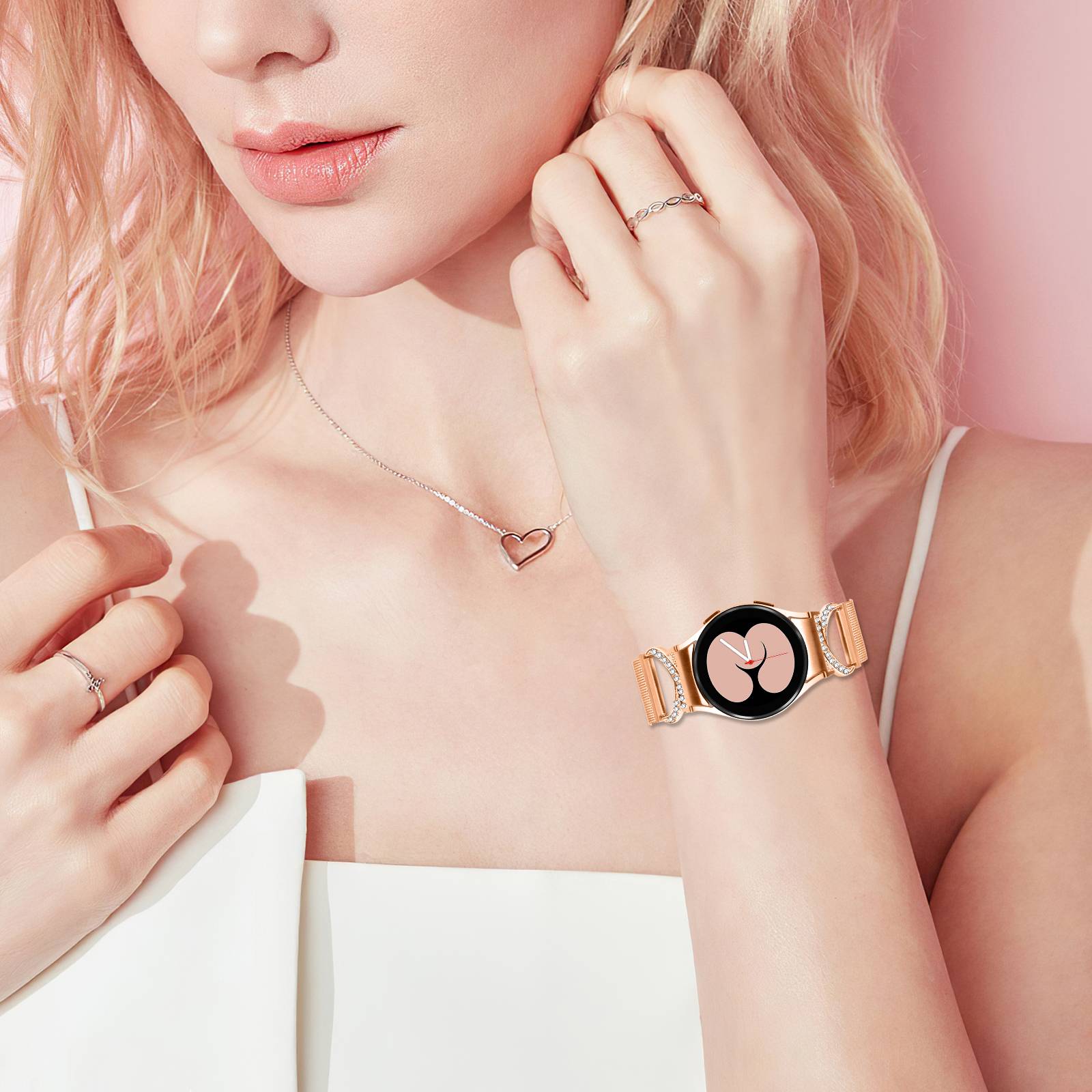 Nahaufnahme einer Frau, die rosafarbenes Schmuck und eine Smartwatch mit einem rosa Blumenzifferblatt vor einem weichen rosa Hintergrund trägt.