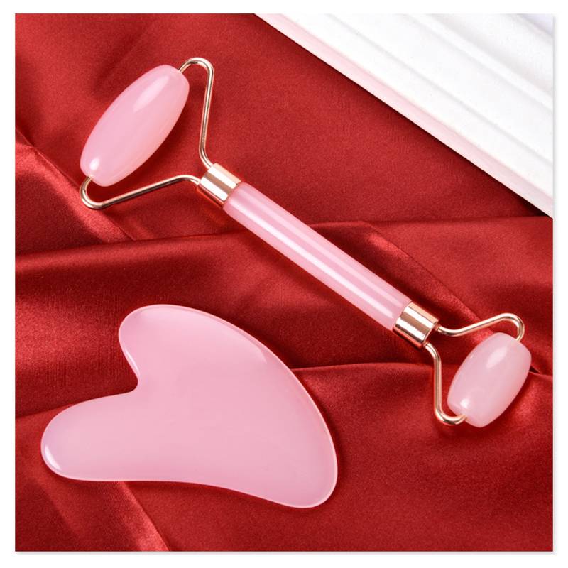 Rosa Gesichtsrolle und herzförmiger Gua-Sha-Stein auf rotem Seide, mit einem weißen gefalteten Tuch in der Ecke.