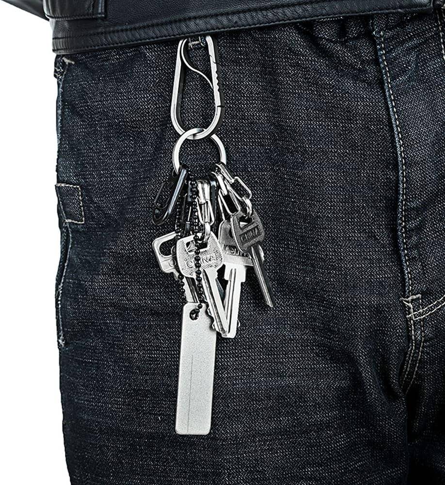 Nahaufnahme von dunkler Jeans mit einer Gürtelschlaufenkarabiner, die ein Bündel Schlüssel und einen weißen rechteckigen Anhänger hält.