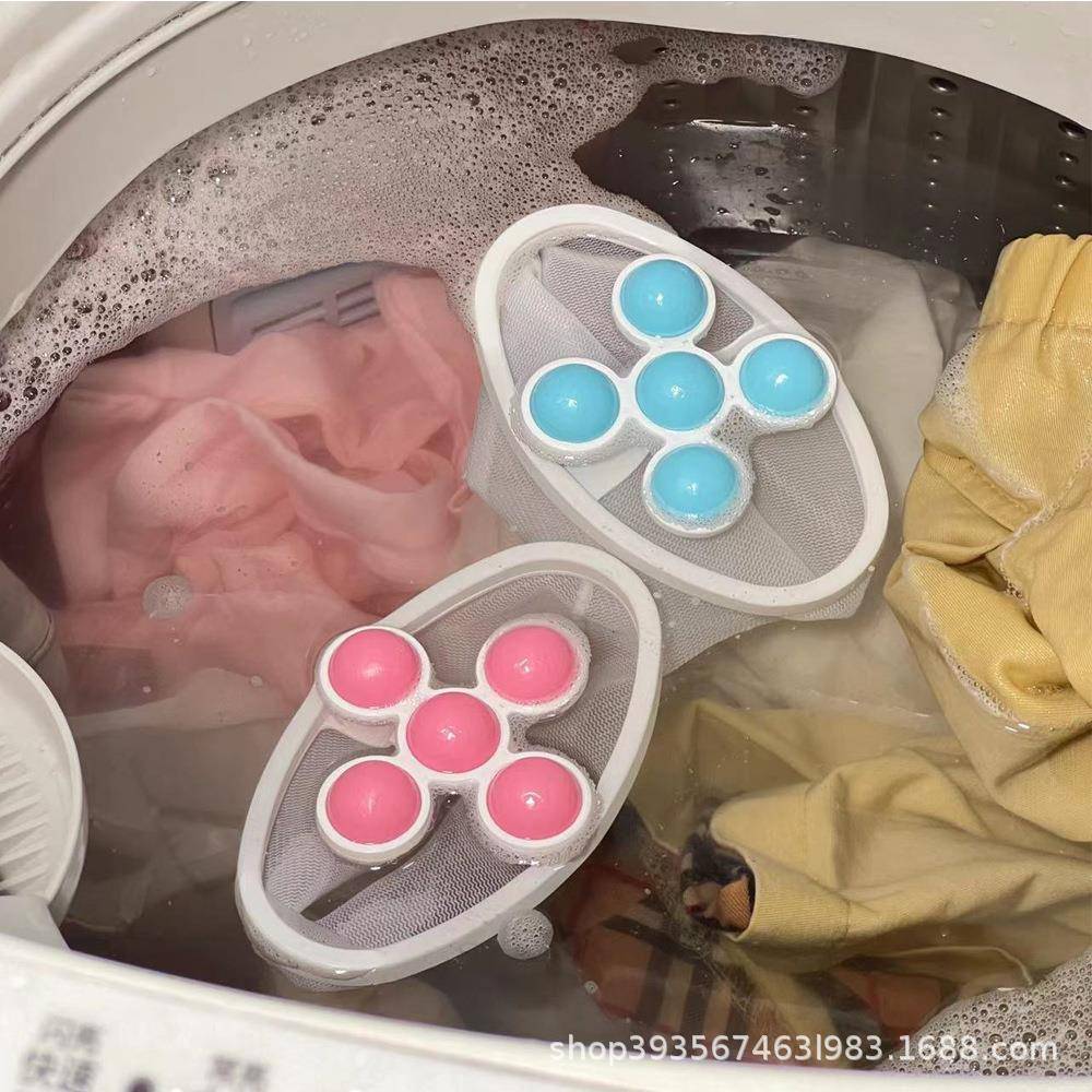 Wäsche, die in einer Waschmaschine mit zwei schwimmenden Mesh-Reinigungspods eingeweicht wird, einer blau und einer rosa, zwischen Kleidung in seifigem Wasser.