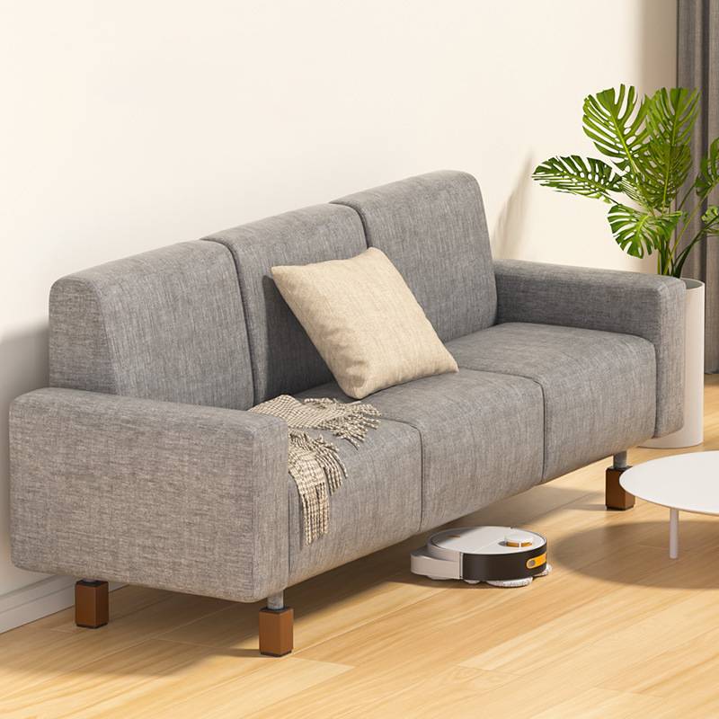 Graues Sofa in einem hellen Wohnzimmer mit einem Kissen und einer Wurfdecke; ein Staubsaugerroboter reinigt den Boden daneben.