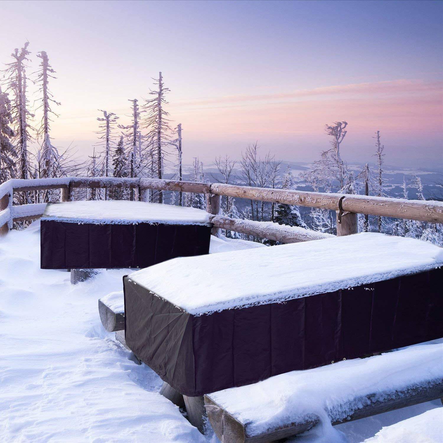 Schneebedeckte Picknicktische auf einer Aussichtsplattform bei Sonnenaufgang, mit raureifbedeckten Bäumen und einem Pastellhimmel im Hintergrund.