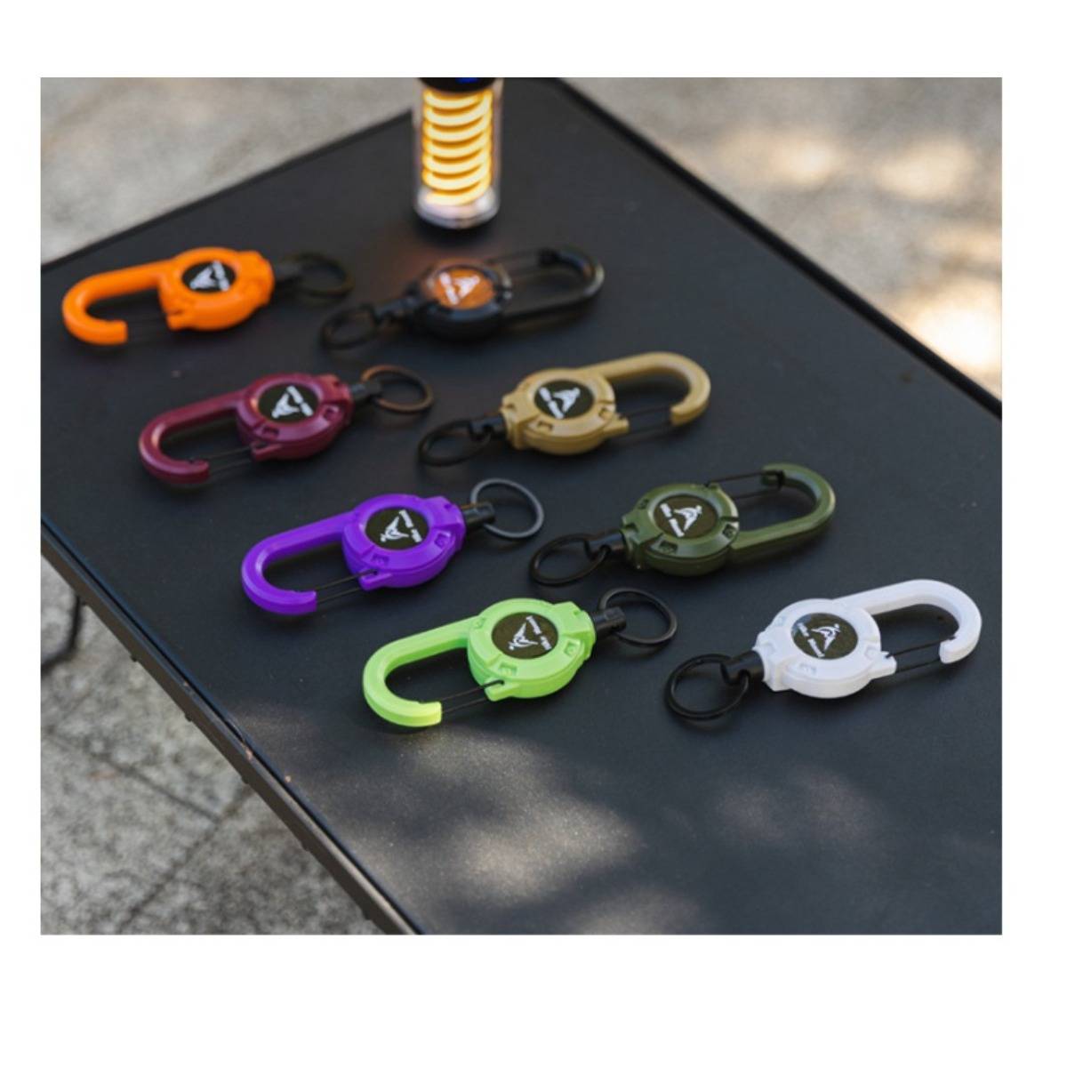 Sortierte bunte Karabiner-Stil-Schlüsselanhänger-Clips, die auf einem schwarzen Tisch im Freien angeordnet sind.