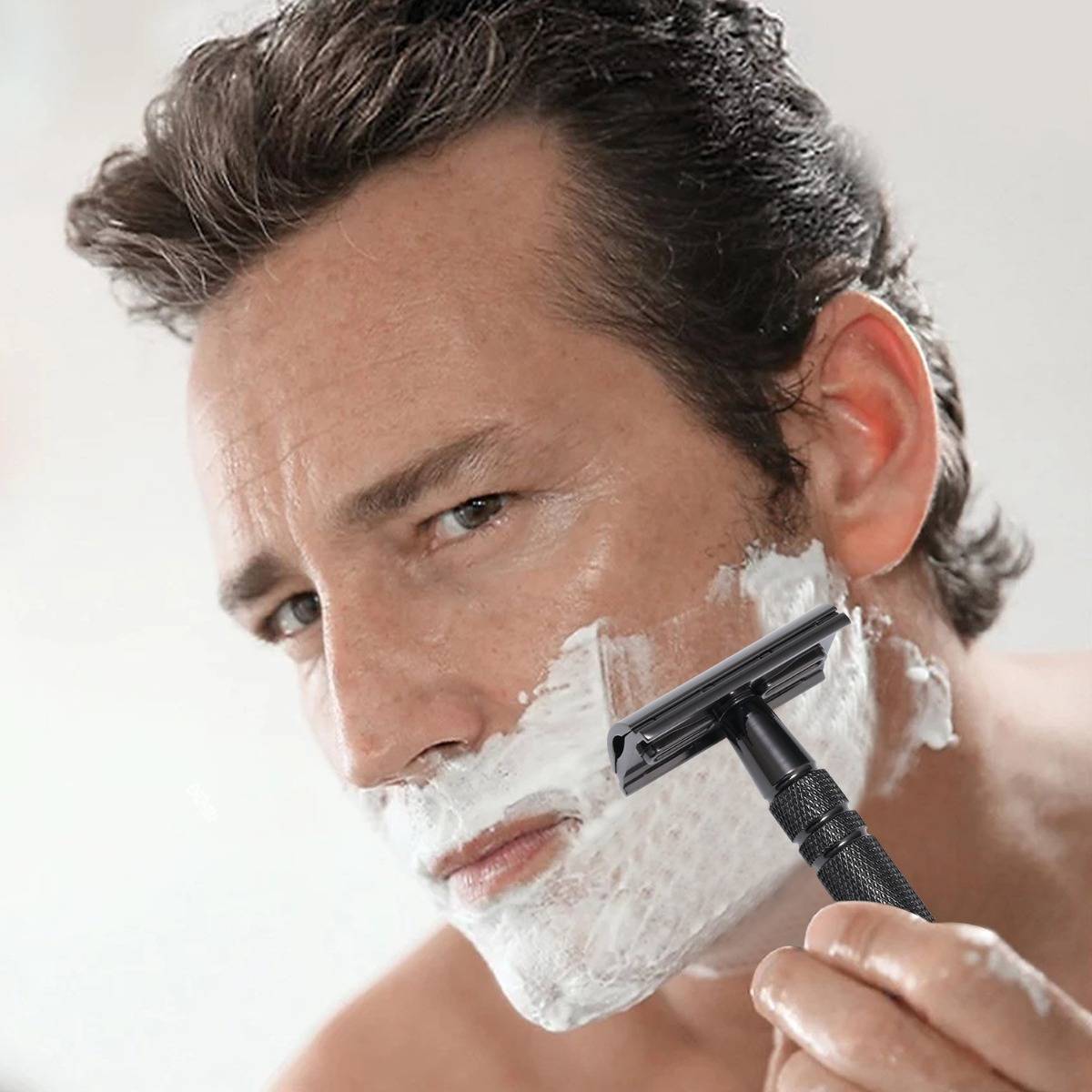 Ein Mann rasiert sein Gesicht mit einem Rasiermesser und Rasierschaum, Nahaufnahme im Badezimmer.