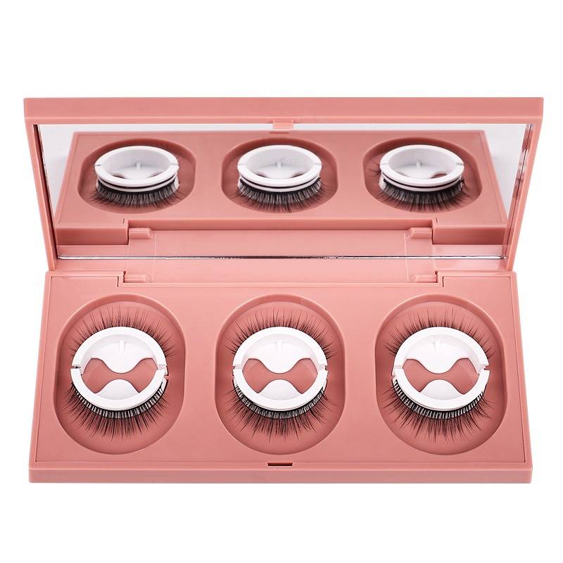 Rosa Makeup-Kompakt mit drei Paar falscher Wimpern in einem verspiegelten Etui, geöffnet vor weißem Hintergrund dargestellt.