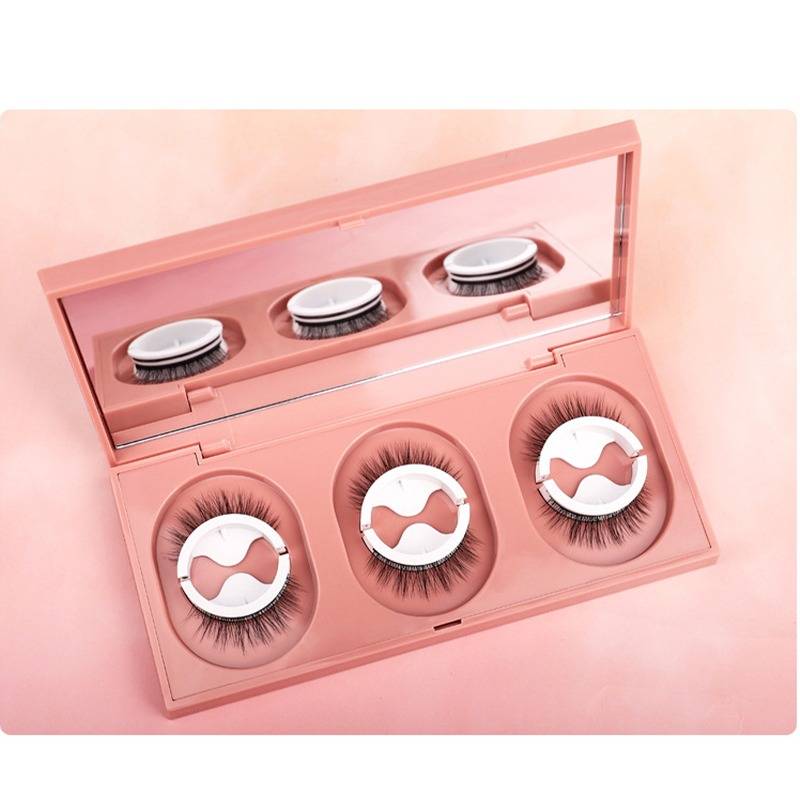Rosa Makeup-Kompakt mit drei Paar künstlichen Wimpern, die in einem Spiegelkasten auf rosa Hintergrund präsentiert werden.
