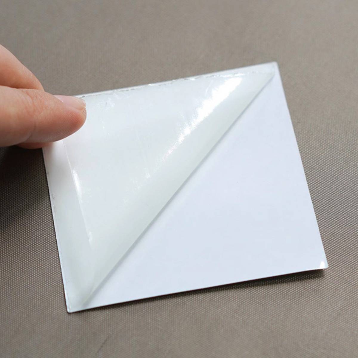 Hand, die eine Ecke eines weißen Klebelabels oder Aufklebers auf einer ebenen Fläche zurückpeelt