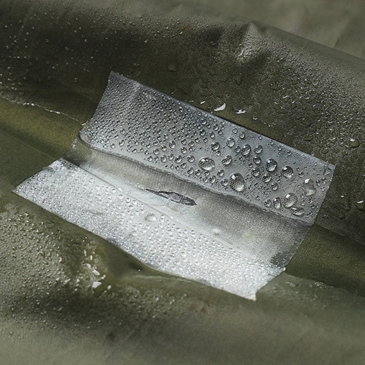 Nahaufnahme einer Stoffoberfläche mit einem rechteckigen Flicken oder Klebeband, das mit Wassertropfen bedeckt ist und eine wasserdichte Reparatur oder Nahtversiegelung suggeriert.