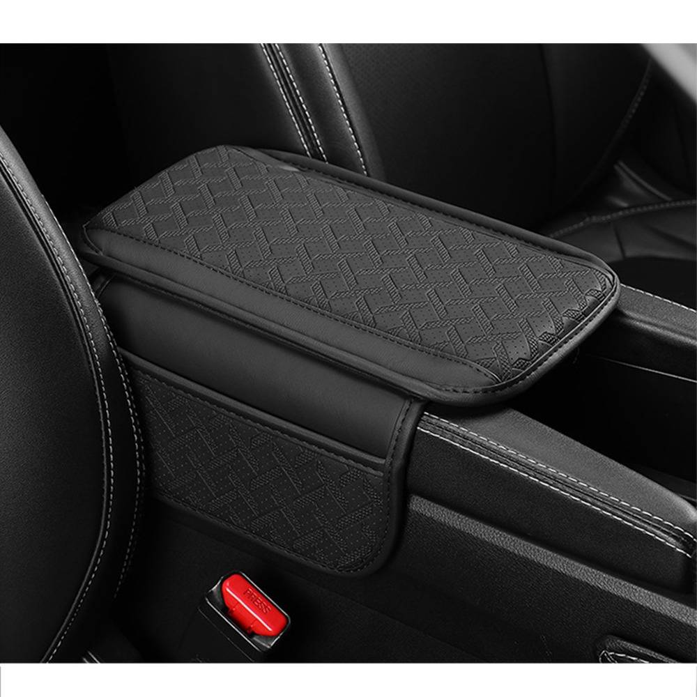 Schwarze gemusterte Armlehnen-Kissenbezug auf einer Mittelkonsole eines Autos, mit sichtbarem rotem Sicherheitsgurt-Schnallenverschluss darunter.