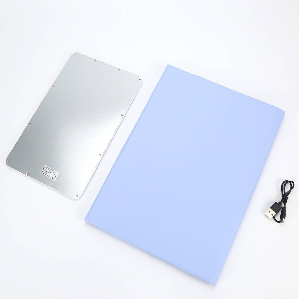 Ein silbernes Metallgerät und eine hellblaue rechteckige Matte liegen auf einer weißen Oberfläche, mit einem USB-Kabel daneben.