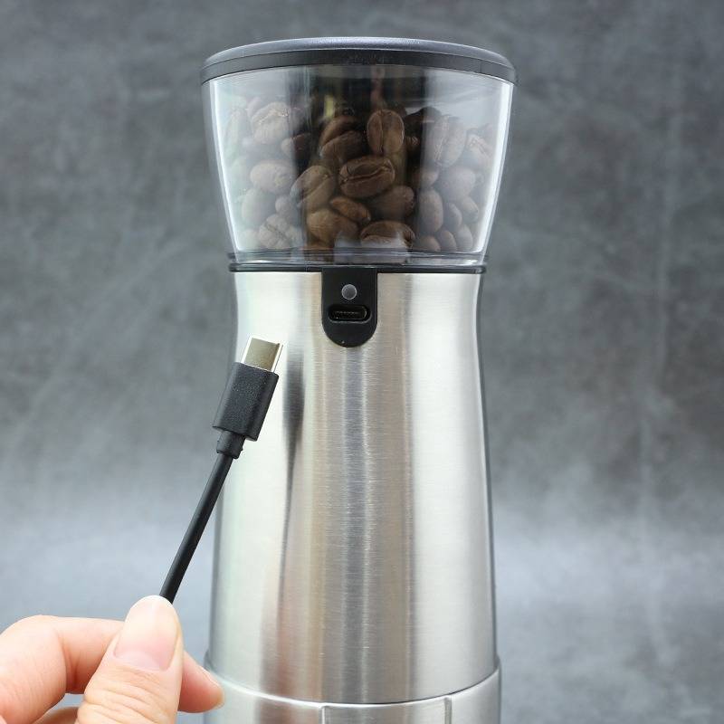 Hand steckt ein USB-C-Kabel in einen Edelstahl-Kaffeemühle, die mit Kaffeebohnen gefüllt ist.