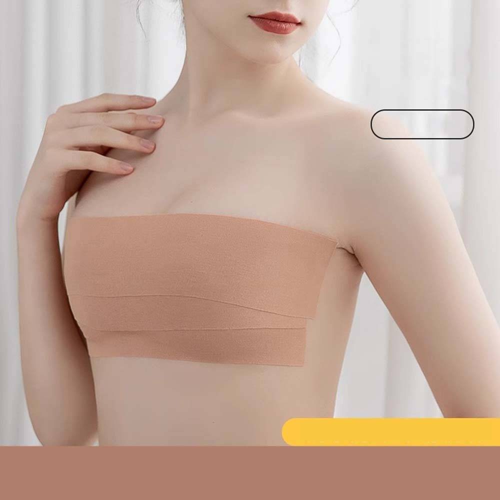Frau, die ein beiges, trägerloses Bandeau-Top trägt und gegen einen hellen Hintergrund posiert.