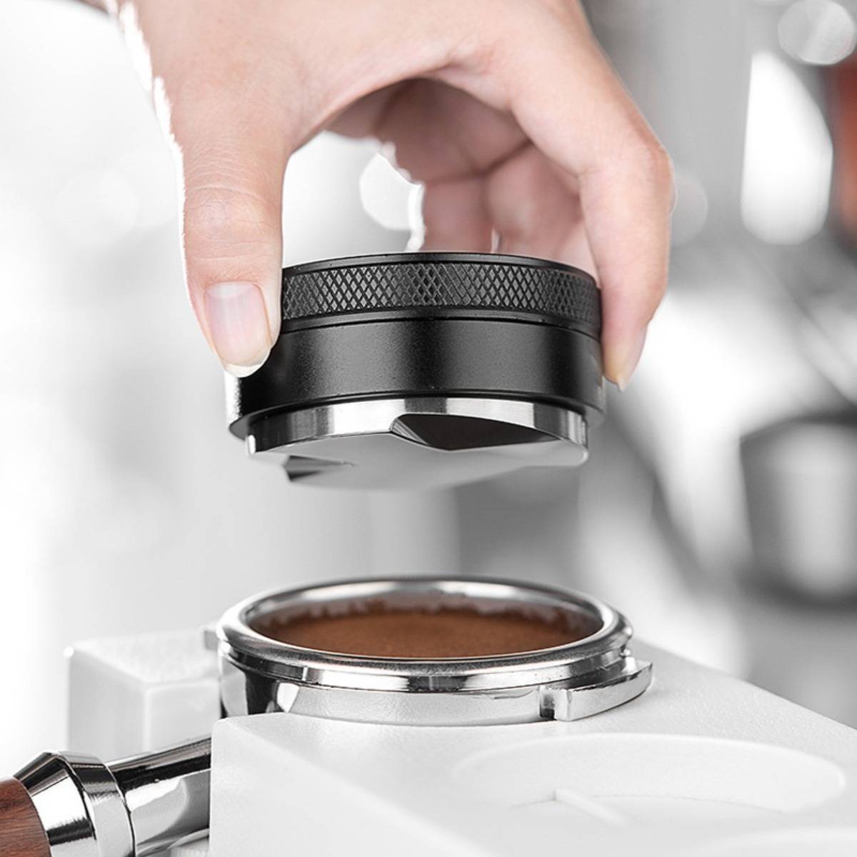 Hand, die einen Kaffeetamper über ein mit gemahlenen Kaffee gefülltes Siebträger-Körbchen platziert, bereitet Espresso in einer Maschine vor.