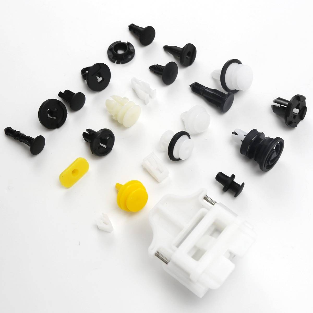 Assortierte Kunststoff-Kfz-Befestigungselemente und Clips, überwiegend schwarz und weiß mit einigen gelben Teilen, verstreut auf weißem Hintergrund.
