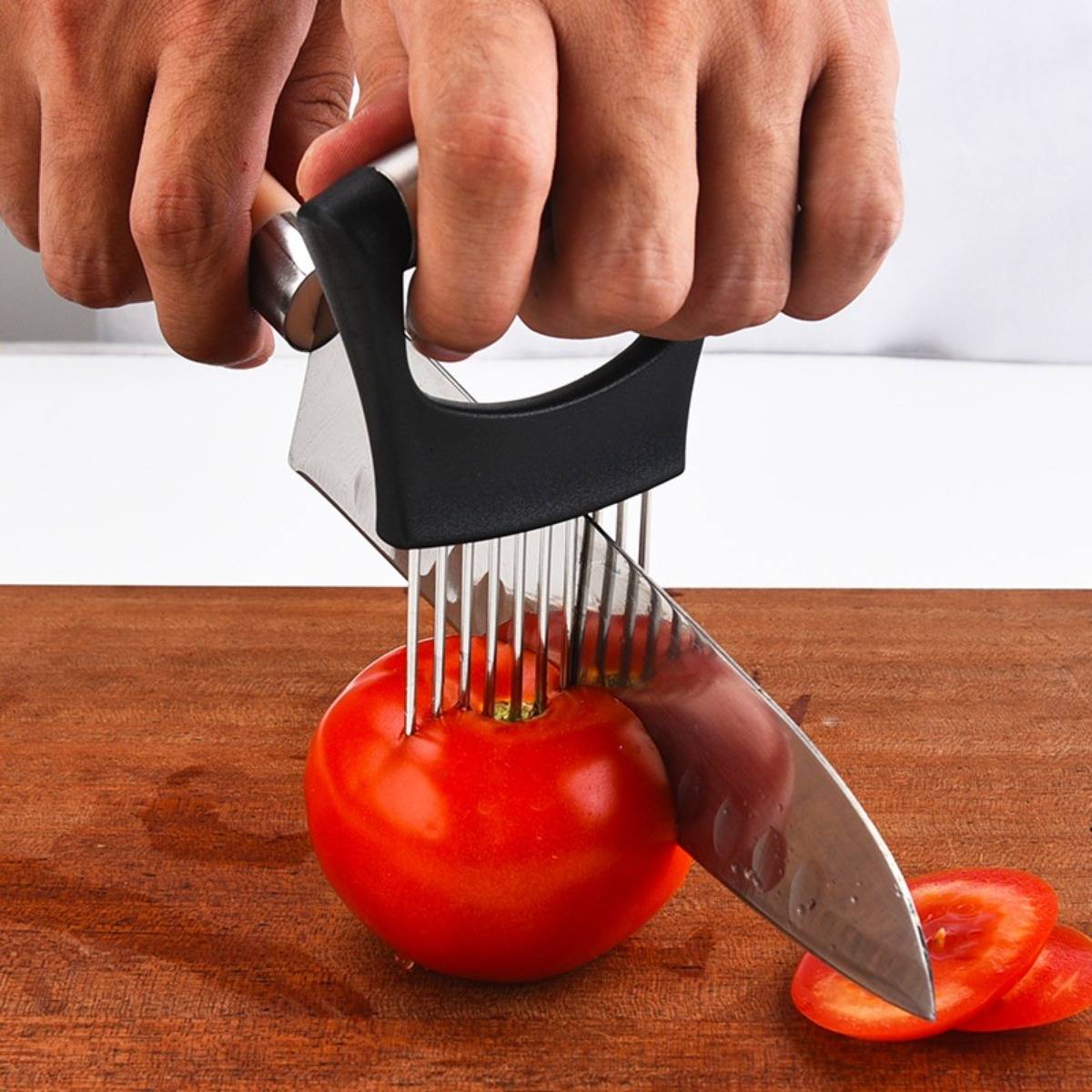 Hände, die einen Tomatenschneider und ein Messer verwenden, um eine rote Tomate auf einem Holzschneidebrett zu schneiden, mit geschnittenen Stücken auf der rechten Seite.