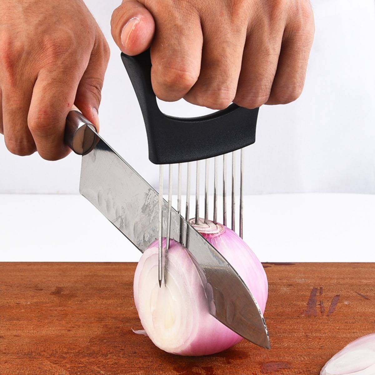 Hände, die ein Messer und einen Zwiebelschneider benutzen, um eine rote Zwiebel auf einem Holzschneidebrett zu schneiden.