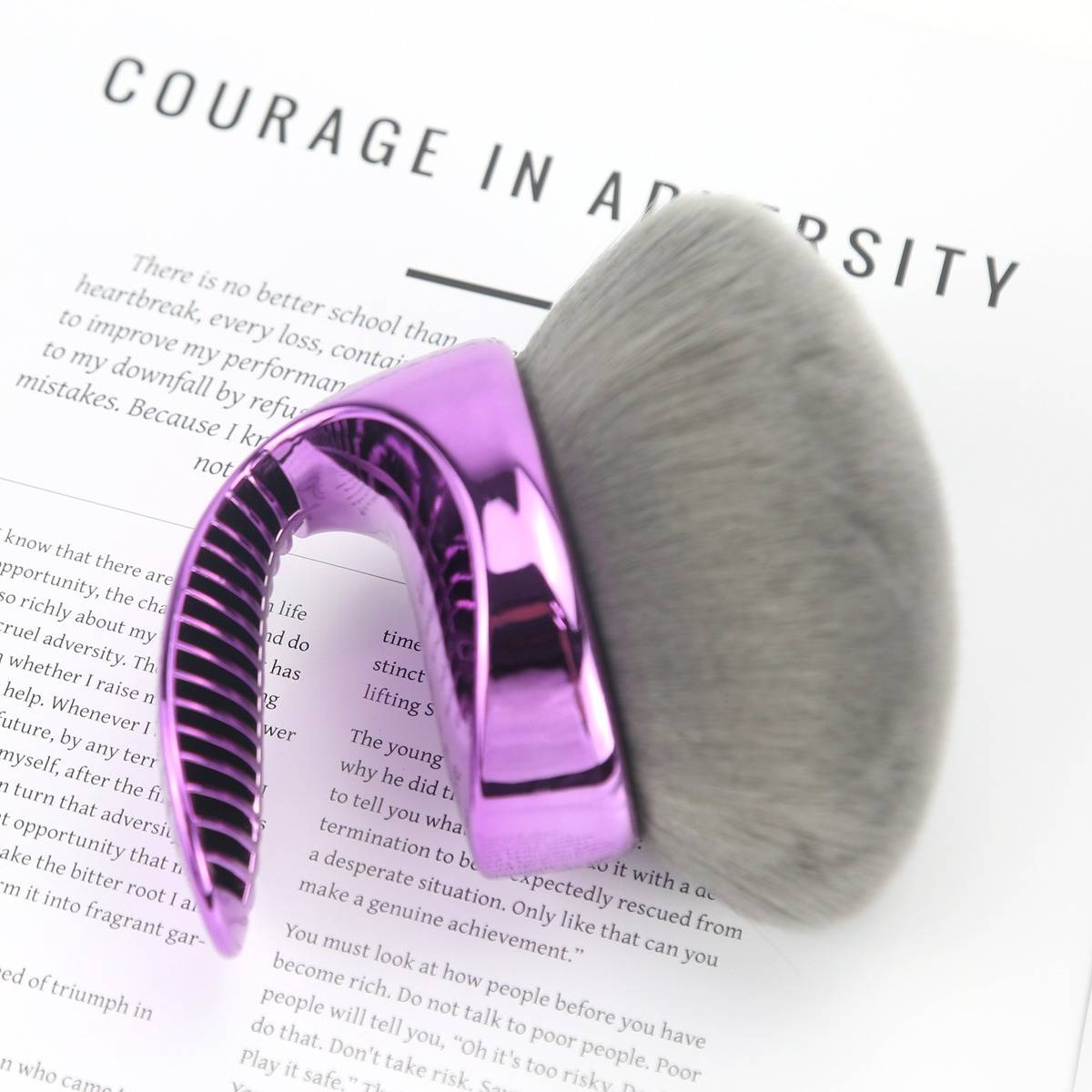 Eine violette und silberne Haarbürste ruht auf einer gedruckten Seite mit dem Titel „MUT IN DER WIDRIGKEITEN".
