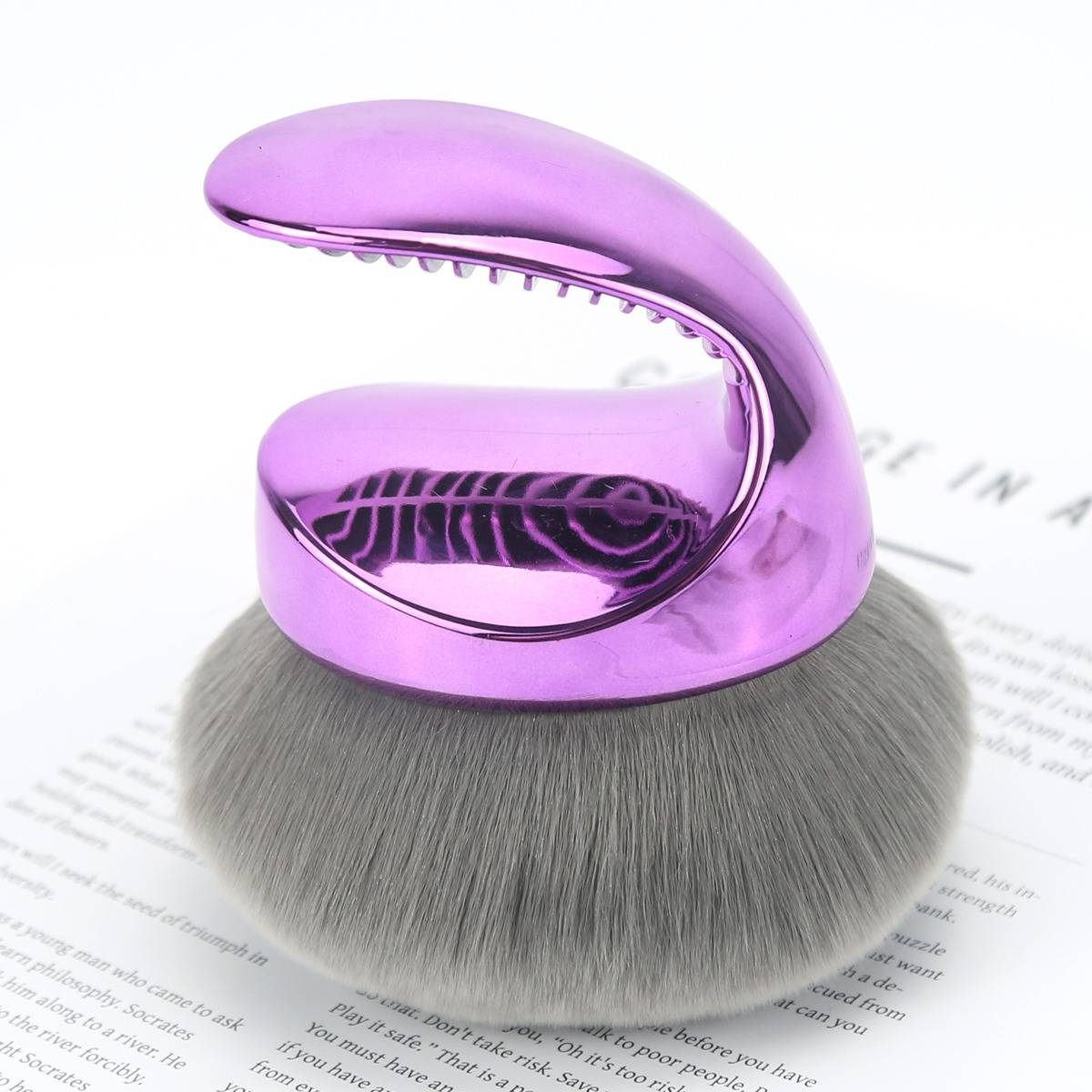 Lila pilzförmiger Make-up-Pinsel mit dichten grauen Borsten auf weißem Seitenhintergrund.