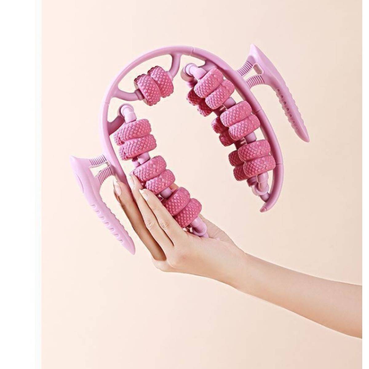 Hand, die einen rosa doppelseitigen Kopfhaut-Massager mit rotierenden Rollen gegen einen hellen Hintergrund hält.