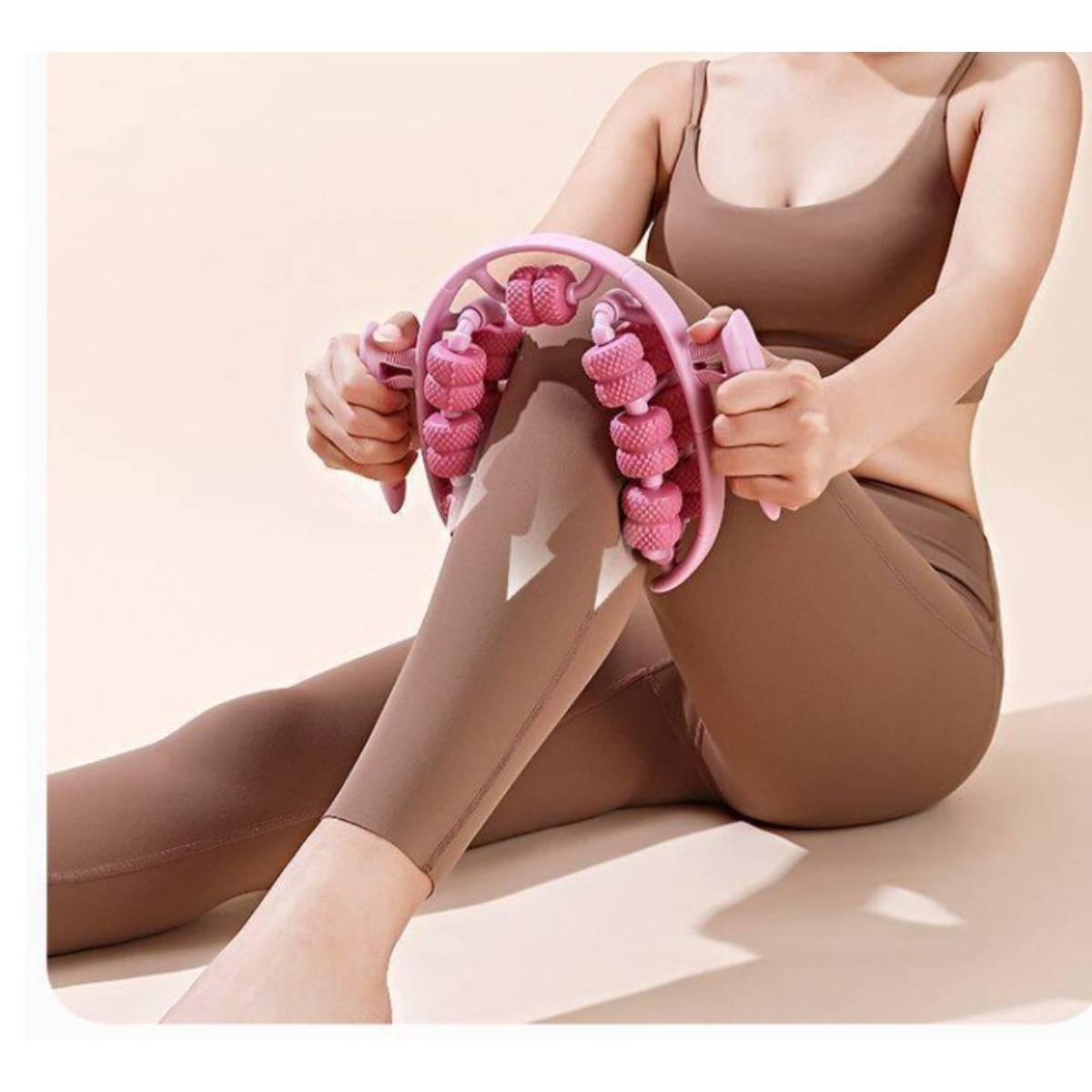 Frau in brauner Sportbekleidung, die auf hellem Hintergrund sitzend eine rosa Beinmassagerolle an ihrem Schienbein und ihrer Wade einsetzt.