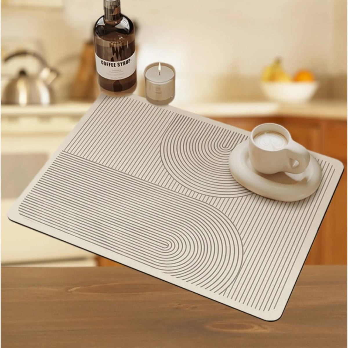 Weißes rechteckiges Platzdeckchen mit schwarzem geschwungenem Linienmuster, auf dem eine Tasse mit Untertasse auf einem Holztisch in einer Küchenumgebung steht.