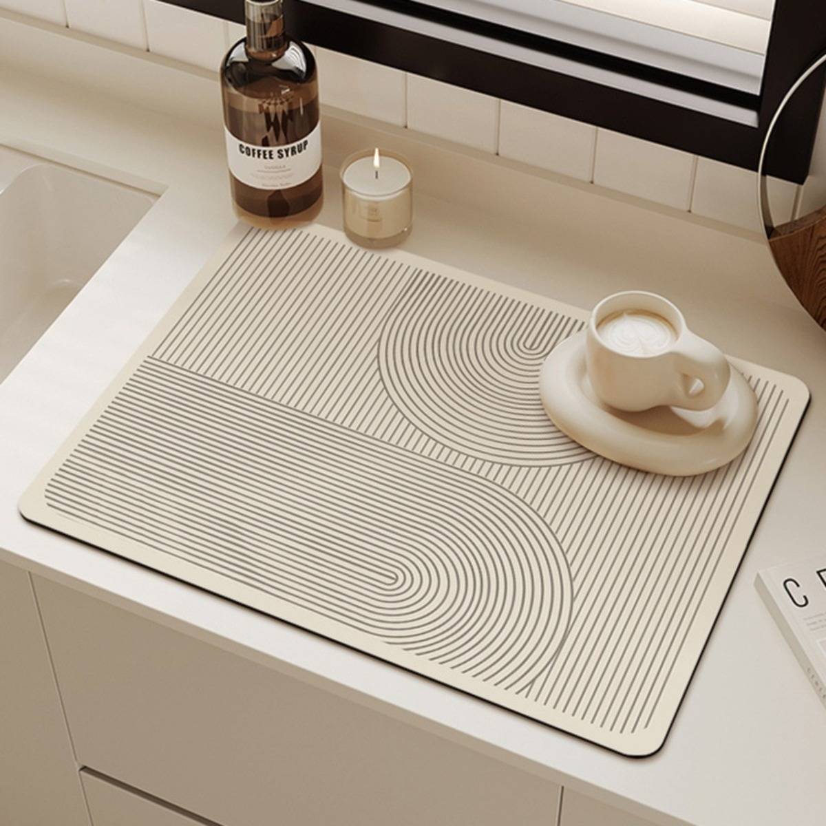 Eine Kaffeetasse auf einer Untertasse sitzt auf einer gemusterten Schreibtischunterlage neben einer Kaffeesirup-Flasche und einer kleinen Kerze auf einer Arbeitsplatte.
